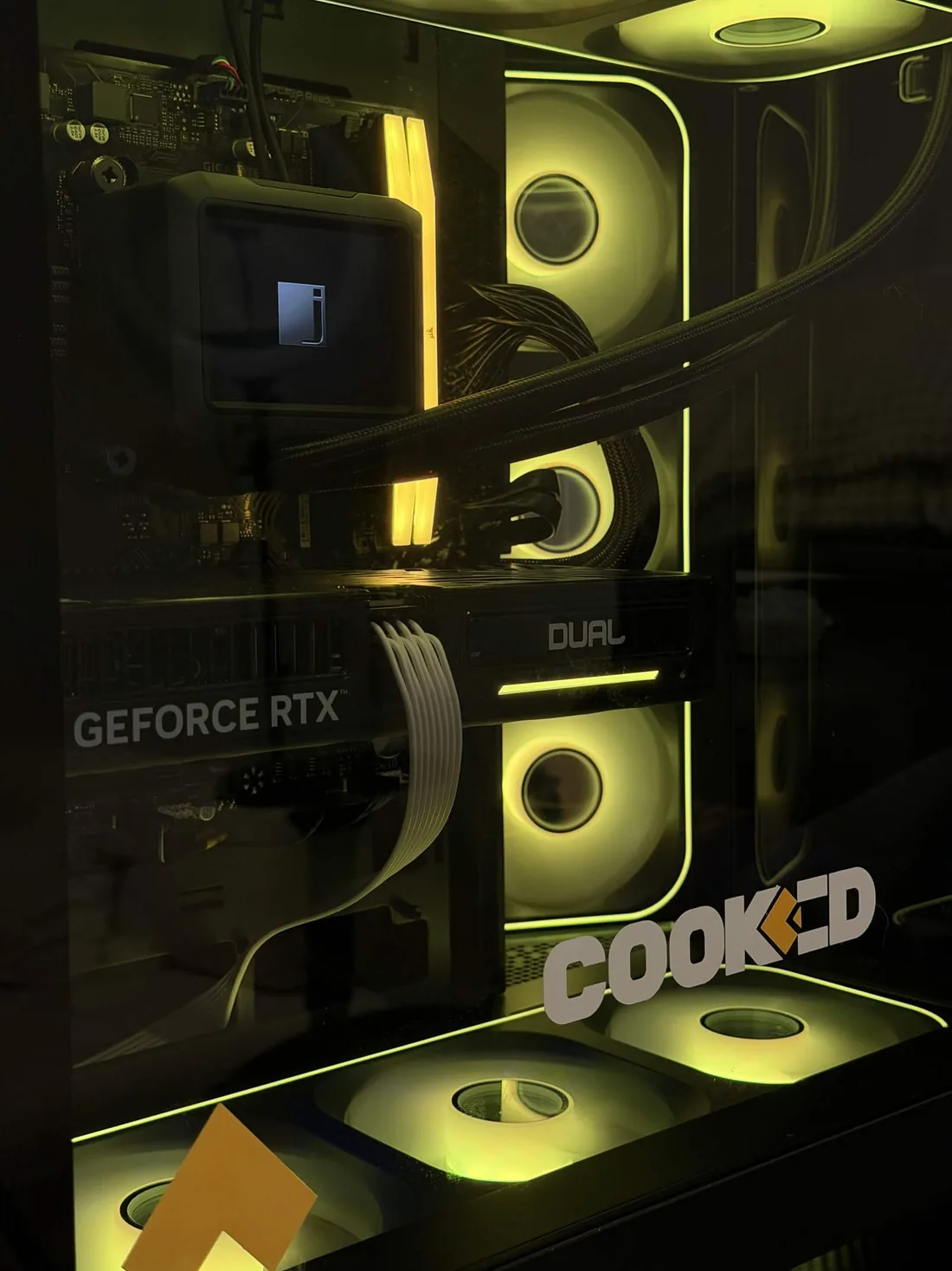 Close-up through the side glass of the giveaway PC: the liquid-cooling pump block, yellow-lit DDR5 memory, an ASUS Dual GeForce RTX graphics card and the COOKED decal on the panel.