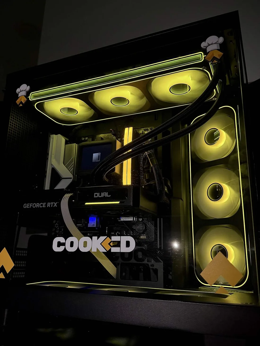 The giveaway PC seen front-on: three radiator fans across the top, three down the front panel and three underneath, all lit yellow behind the glass, with the COOKED decal centred.
